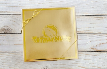 gold signature 4-choice gift box with gold on gold totally nutz logo, box on a light wood background